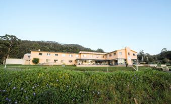 a large orange building surrounded by a lush green field , with mountains in the background at Lufra Hotel and Apartments