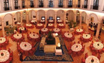 a large , elegant banquet hall with multiple round tables set for dinner , surrounded by pillars and arches at Parador de Lerma