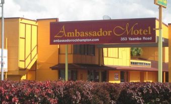 the ambassador hotel is a yellow building with red trim , surrounded by a well - maintained garden at Ambassador Motel