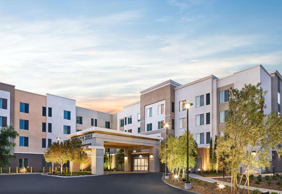a modern , multi - story apartment building with a hotel entrance and trees surrounding it , under a blue sky with clouds at Homewood Suites by Hilton Aliso Viejo Laguna Beach