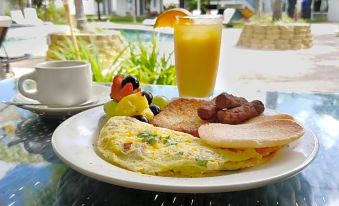 a breakfast plate with an omelette , fruit , and a glass of orange juice on a table near a pool at Solace by the Sea