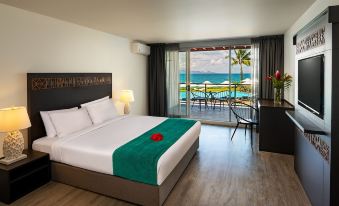 a hotel room with a king - sized bed , a television , and a balcony overlooking the ocean at The Pearl South Pacific Resort