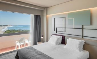 a hotel room with a large bed and a view of the ocean through a window at Axis Ofir Beach Resort Hotel