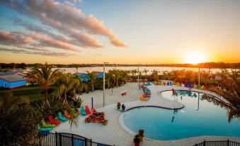 a large outdoor swimming pool surrounded by palm trees , with a beautiful sunset in the background at Legoland Beach Retreat