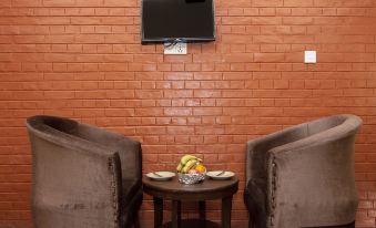 a living room with a brick wall , two brown chairs , a small table with a bowl and fruit , and a flat - screen tv mounted at Hotel Marigold