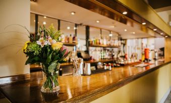 a wooden bar with a vase of flowers on it , surrounded by bottles and glasses at The Stratton House Hotel