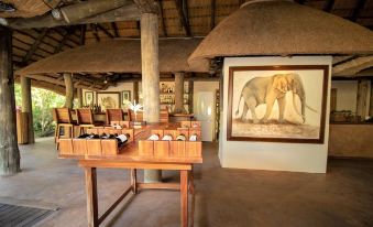 a room with wooden tables and chairs , a table with bottles on it , and an elephant painting on the wall at Tembe Elephant Park