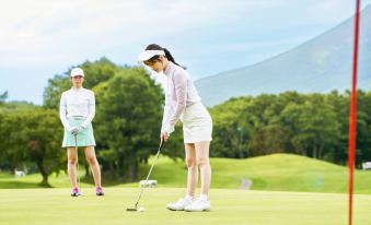 two women are standing on a golf course , one of them is holding a golf club and preparing to putt at Hakodate-Onuma Prince Hotel