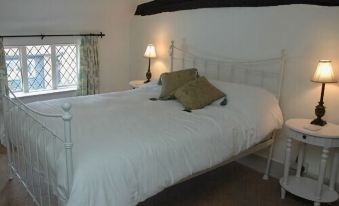 a cozy bedroom with white bed , two pillows , and a lamp on the nightstand , next to a window with curtains at The Brocket Arms