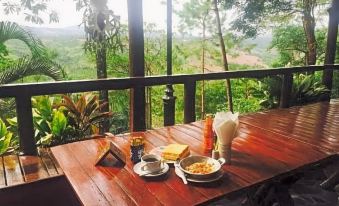 a wooden table on a balcony overlooking a beautiful view of the jungle , with breakfast items such as coffee and pastries at Phu Pha Nam Resort