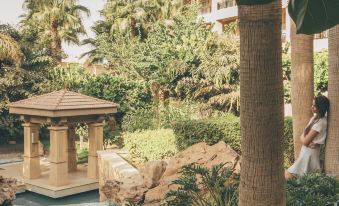 a woman in a white dress is standing near a pond , surrounded by lush greenery and a gazebo at Dusit Thani LakeView Cairo