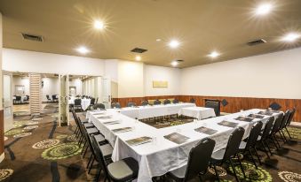 a large conference room with multiple tables , chairs , and a dining area , decorated with white tablecloths and green carpet at Nightcap at Waltzing Matilda Hotel