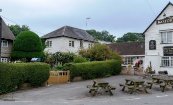 a white house with a black roof is surrounded by greenery and has picnic tables in front at The Barford Inn