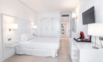 a white bedroom with a double bed , a dresser , and a tv mounted on the wall at Landmar Costa Los Gigantes