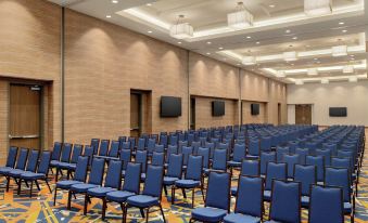 a large conference room with rows of blue chairs arranged in a semicircle , and a tv mounted on the wall at Embassy Suites by Hilton South Jordan Salt Lake City