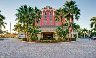 a large red building with palm trees in front of it , creating a tropical atmosphere at Embassy Suites by Hilton Fort Myers Estero