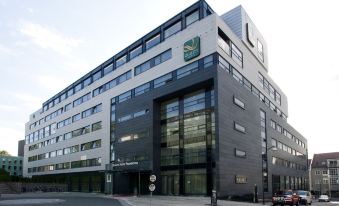 a large modern building with a green logo on the front and a street scene in front at Quality Hotel Fredrikstad