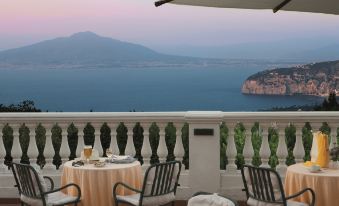 a table with a glass of wine and two chairs on a balcony overlooking the ocean at Hotel Jaccarino