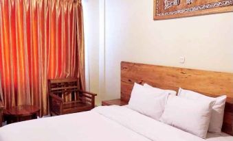 a bedroom with a wooden bed , white sheets , and a chair near a window with orange curtains at Hotel Grand Papua Fakfak