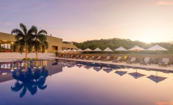 a large outdoor swimming pool surrounded by lounge chairs and umbrellas , with the sun setting in the background at Hotel Waya Guajira