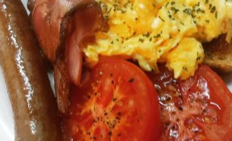 a plate of food , consisting of scrambled eggs , bacon , sausage , tomatoes , and a sausage at Sandhurst Motor Inn Bendigo