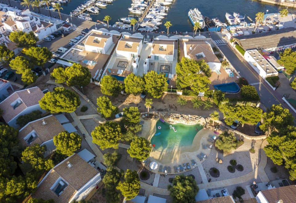 an aerial view of a resort with multiple buildings , a pool , and boats in the harbor at Lago Resort Menorca Casas del Lago