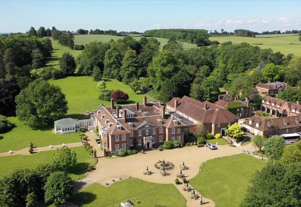 aerial view of a large brick mansion surrounded by trees and grass , with a fountain in the foreground at Chilston Park Hotel