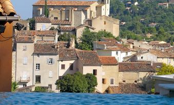 a picturesque village with a church on top of a hill , surrounded by lush greenery and a body of water at La Roque