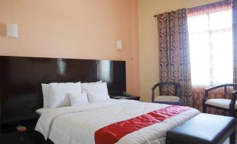 a well - arranged hotel room with a white bedspread , red and black striped pillow , and a window with curtains at Syafira Hotel Langgur