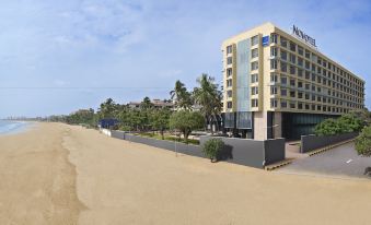 a beach with a sand dune , palm trees , and a hotel building in the background at Novotel Mumbai Juhu Beach