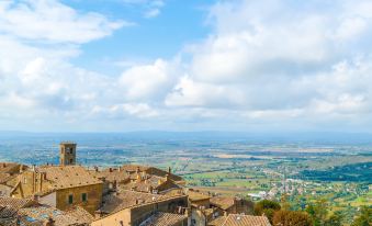 a view of a village nestled in the mountains with a cloudy sky and green fields at Monastero di Cortona Hotel & Spa