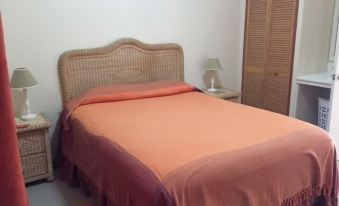 a neatly made bed with a pink blanket and a wicker headboard is in a room with a wooden cabinet at Hillside Apartments