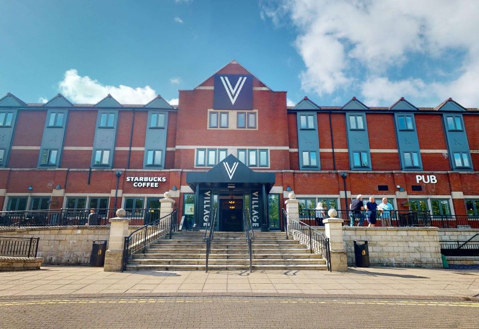 a brick building with a starbucks sign on the front , located in a city setting at Village Hotel Cardiff
