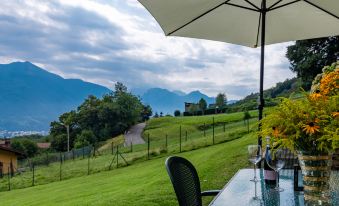 a dining table with a white umbrella and chairs on a grassy hillside overlooking a mountainous landscape at Martina