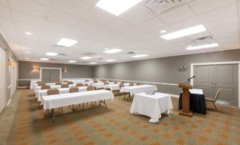 a large conference room with white tables , chairs , and a podium , set up for an event or meeting at Ramada by Wyndham New Iberia
