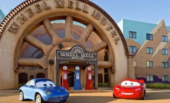 two cars are parked in front of a building with a wheel well hotel sign at Disney's Art of Animation Resort