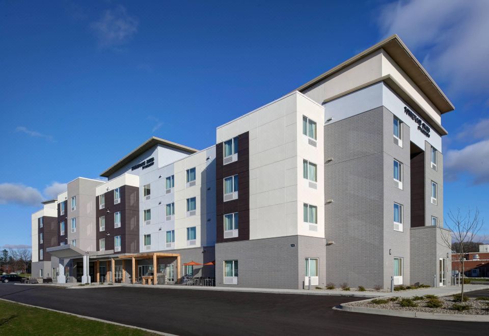 a modern hotel building with a large parking lot and clear blue skies in the background at TownePlace Suites Grand Rapids Airport