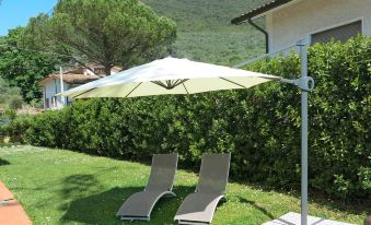a man sitting on a lounge chair under an umbrella in a grassy backyard , next to a house at La Rondine