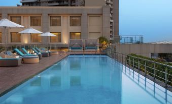 an outdoor swimming pool surrounded by lounge chairs and umbrellas , with a building in the background at DoubleTree by Hilton Agra