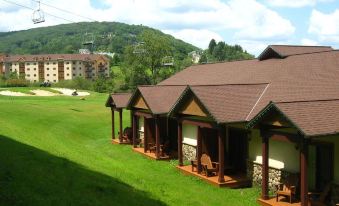 a row of small wooden cabins situated on a grassy hillside , with a mountain in the background at The Inn at Holiday Valley
