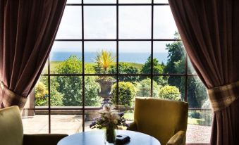 a table with a vase of flowers is placed in front of a large window overlooking the ocean at Old Manor Hotel