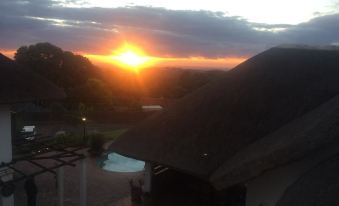 a beautiful sunset over a thatched - roof house , with the sun setting behind a cloudy sky at Summerhill Guest Estate