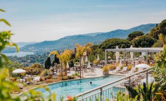 a large outdoor pool surrounded by lounge chairs and umbrellas , with a beautiful view of the mountains in the background at Hotel la Villa Douce