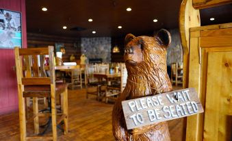 "a wooden bear statue with a sign that reads "" please wait to be seated "" in a restaurant" at Daniels Summit Lodge