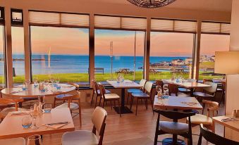 a dining room with a view of the ocean , featuring several tables and chairs arranged for a meal at Bayview Hotel