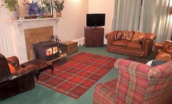 a cozy living room with a fireplace , a couch , a chair , and a tv . also a dining table in the room at Rigg House B&B
