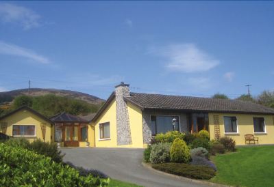 a yellow house with a brown roof and a chimney is surrounded by greenery , bushes , and flowers at Highlands