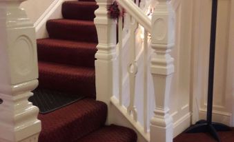 a white staircase with a red carpet and a white railing , leading up to the second floor of a building at Tudor House