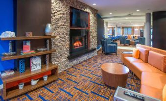 a modern lounge area with a stone fireplace , wooden shelves , and an orange couch , all set against blue - carpeted flooring at Courtyard by Marriott Montgomery Prattville