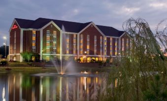 a large building with a fountain in front of it , surrounded by trees and water at Hilton Garden Inn Jackson/Madison
